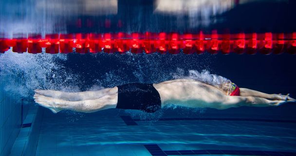 Ένας άνδρας κολυμβητής προπονείται στην πισίνα, σε εσωτερικούς χώρους. Υποβρύχια άποψη των κινήσεων κολύμπι λεπτομέρειες. Υγιεινός τρόπος ζωής, δύναμη, ενέργεια, σπορ κίνημα έννοια. - Φωτογραφία, εικόνα