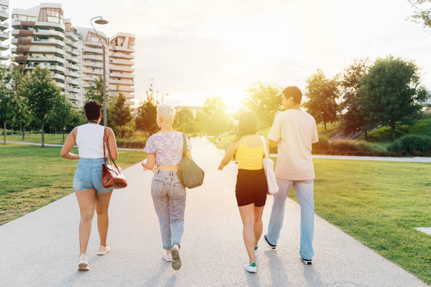 Back view group of multiethnic young tourist friends outdoor having fun walking together chatting enjoying good company sightseeing - Photo, Image