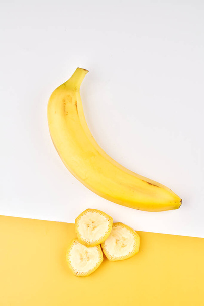 Banana creative background. Yellow and white backdrop with whole, peeled, sliced bananas - Foto, afbeelding