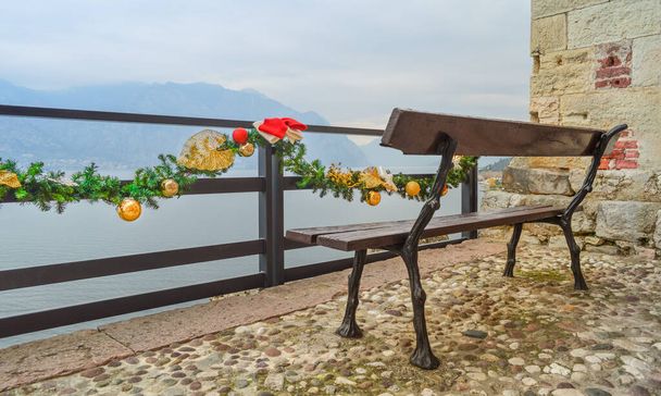 Panchina nel castello Scaligero sul ponte di osservazione con vista sulle montagne e sul Lago di Garda. Decorazioni natalizie e ornamento sulla ringhiera della recinzione. - Foto, immagini
