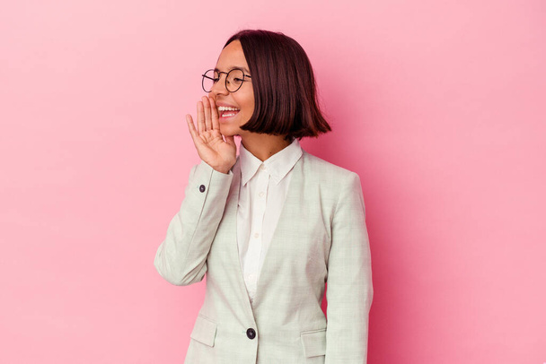 jong gemengd ras vrouw het dragen van een groen pak geïsoleerd op roze achtergrond schreeuwen en houden palm in de buurt van geopende mond. - Foto, afbeelding