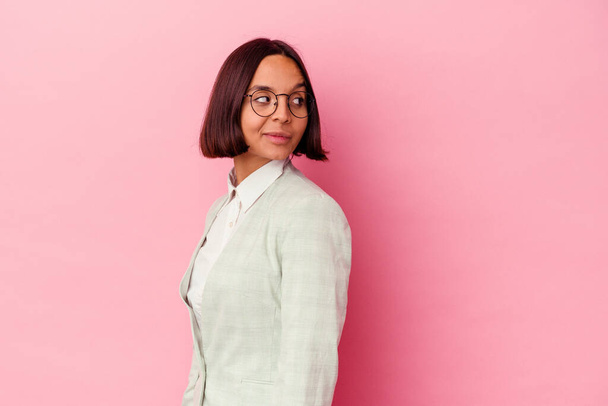 Young mixed race woman wearing a green suit isolated on pink background looks aside smiling, cheerful and pleasant. - Foto, imagen