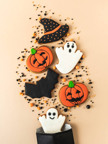 Various Halloween gingerbread cookies - Jack O'Lanterns, black hat, ghosts, bat and sugar sprinkles scattering of paper bag on beige background. Halloween concept. Top view. Copy space - Photo, Image