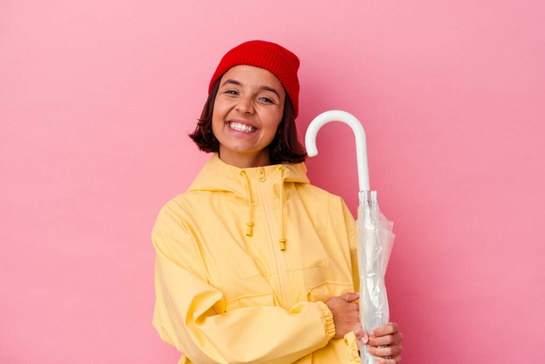 Young mixed race woman holding an umbrella isolated on pink background laughing and having fun. - Фото, изображение