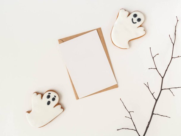 Empty white postcard and craft envelope and Halloween gingerbread cookies ghosts on white background. Halloween concept. Top view. Copy space - Photo, image