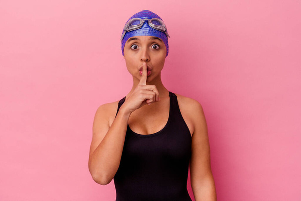 Junge Schwimmerin gemischt Rennen Frau isoliert auf rosa Hintergrund halten ein Geheimnis oder bitten um Schweigen. - Foto, Bild