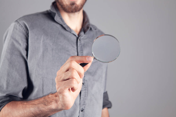 man holding a magnifying glass on gray background - Foto, Imagen