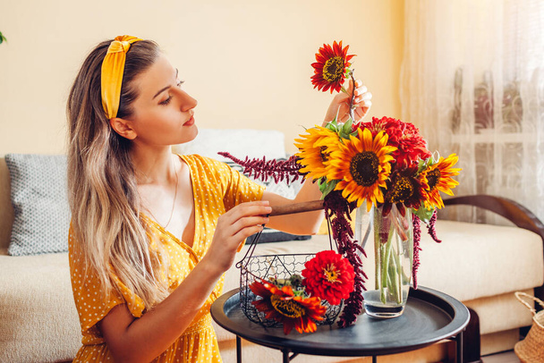 Gros plan sur l'arrangement du bouquet. Femme met tournesols et zinnias dans un vase sur la table à la maison. Fleurs fraîches jaune automne brun rouge. Intérieur et décor - Photo, image