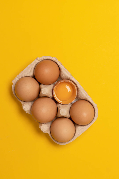 Brown chicken eggs and one broken egg with yolk in eco basket on a yellow background. Natural healthy food - 写真・画像