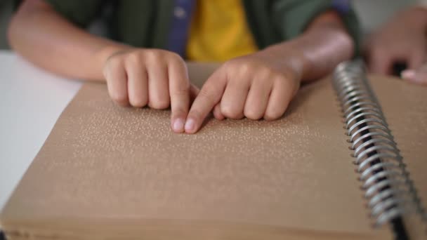 kid handen lezen braille boek met symbolen lettertype voor visueel gehandicapten close-up, moeder zit in de buurt en helpt blinde zoon aan tafel binnen - Video