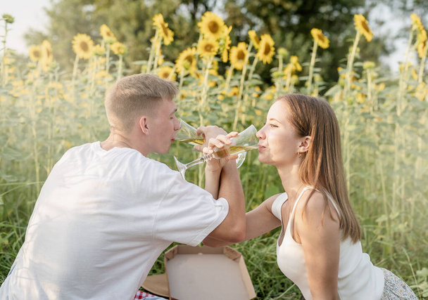 Jesienna natura. Zabawny i pewny siebie. młody nastolatek para piknik na słonecznik pole w zachód słońca picie szampan toasting - Zdjęcie, obraz