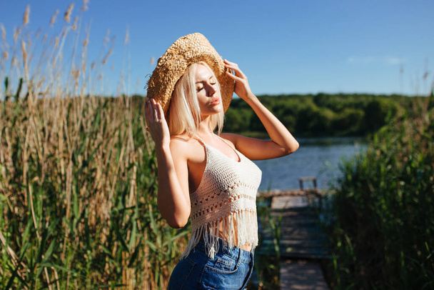 Mooi model meisje poseren op het veld genieten van de natuur buiten in een strohoed. schoonheid blond jong vrouw met lange rechte blond haar close up portret. - Foto, afbeelding