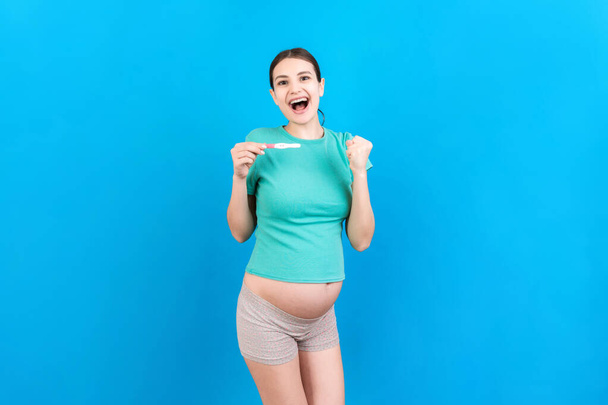 pozitív terhességi teszt két csík ellen boldog terhes nő has színes háttér. Jövőbeli anya szürke ruhában. Terhességi meglepetés. Fénymásolási hely. - Fotó, kép