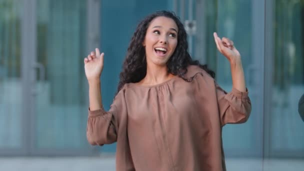 Gelukkig actieve vrouwelijke danser Spaanse vrouw meisje met lang haar mooi dame dansen met handen actief bewegende armen naar muziek buiten staande in de buurt van glazen gebouw dansen vieren weekend vakantie - Video