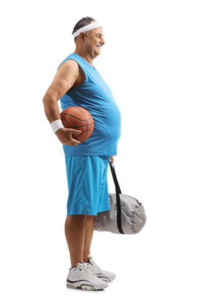 Full length profile shot of a mature man in a blue jersey holding a basketball and a sports bag isolated on white background - Foto, Imagem