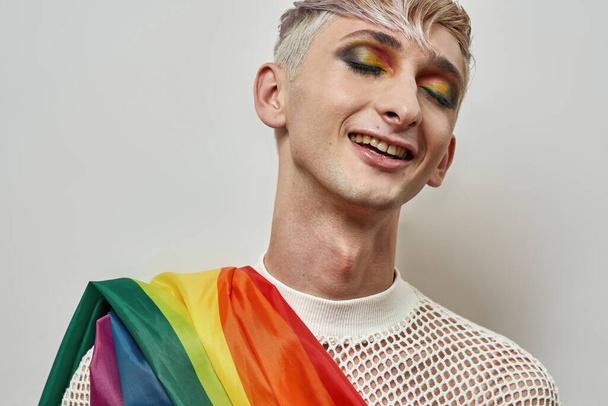 Portrait of happy young transgender with bright dark night party makeup on and colorful rainbow lgbtq flag posing with eyes closed isolated over white background - Fotó, kép