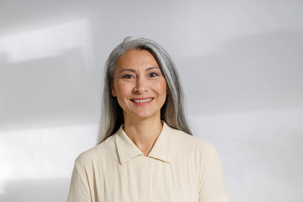 Retrato de mulher de cabelos grisalhos bonita em blusa bege no fundo claro - Foto, Imagem