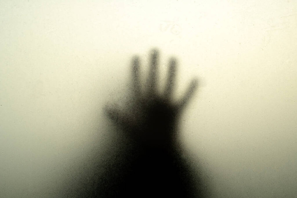 Hand zwart silhouet achter misted glas in de schaduw - Foto, afbeelding