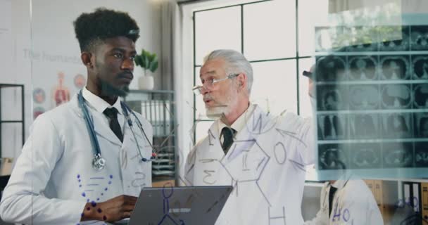 Attractive serious respected skilled bearded professor of medical university talking to his confident african american student in clinic lab and explaining x-ray scan - Materiał filmowy, wideo