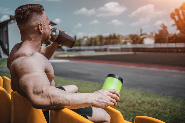 muscular athlete male drinking protein whey cocktail and hold shaker outdoor - Fotó, kép
