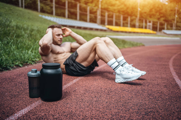 protein whey drink in black container and muscular athlete exercising outdoor - 写真・画像