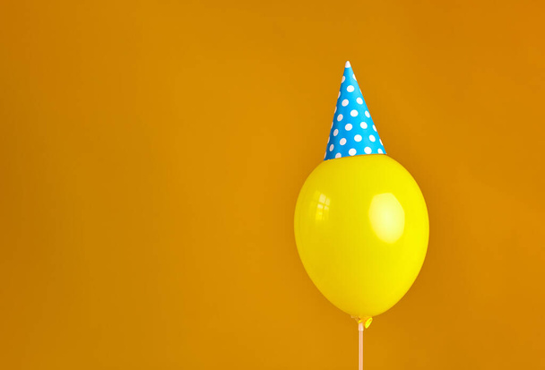 Verjaardagsfeest gele ballon met blauwe feestmuts geïsoleerd op oranje achtergrond - Foto, afbeelding