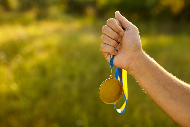 Winner hand holding gold medal with ribbon. Golden medal is medal awarded for highest achievement for sport or business. Success Awards concept - Photo, Image