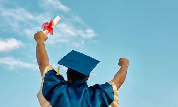 Οπίσθια όψη του ανθρώπου Ρίχνει τα χέρια επάνω ένα πιστοποιητικό και Cap στον αέρα, Ημέρα αποφοίτησης στο φόντο του ουρανού - Φωτογραφία, εικόνα