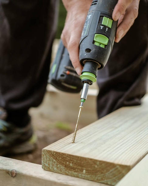 A vertical shot of a Caucasian man working with a drill, building outdoors - Photo, image
