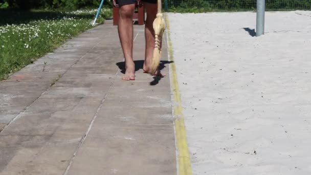 O contínuo de camisa vermelha limpa a areia do passeio com uma vassoura. Um rapaz de 20 anos varre o pavimento. - Filmagem, Vídeo