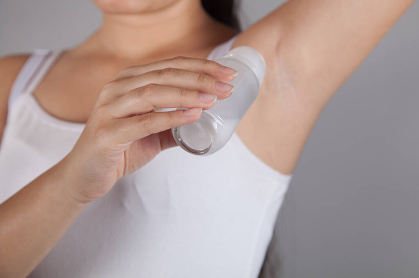 Woman applying deodorant, gray background. - Foto, Imagem