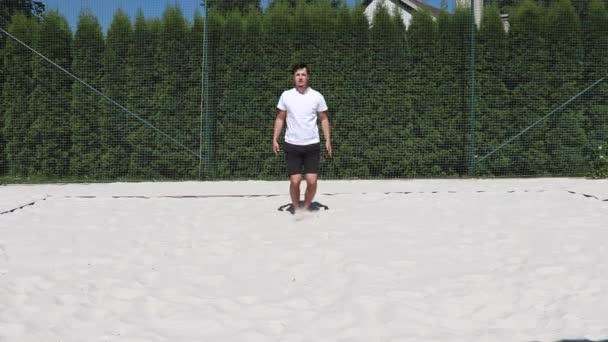 Joven entrenador demuestra la correcta ejecución de un gato saltando en una cancha de voleibol de playa en tiempo soleado - Metraje, vídeo