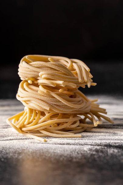 Italian pasta nest. Uncooked spaghetti nest and flour on black table. - Фото, изображение