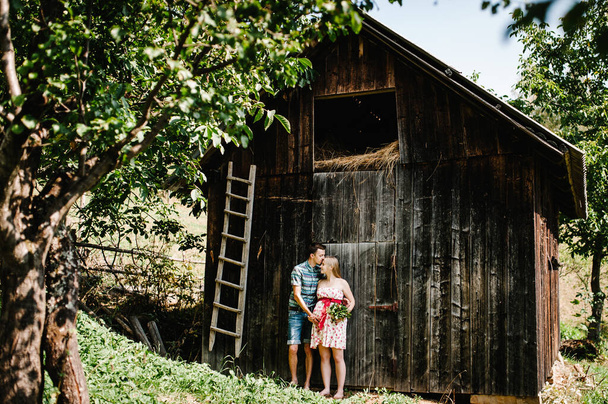 In waiting the baby, babe. A happy family. A pregnant woman with her beloved husband. Round belly. Parenthood. The sincere, best and tender moments. Husband kissing pregnant wife in front of old barn - Foto, afbeelding