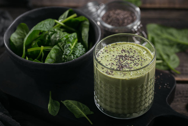 Szklanka domowego zdrowego zielonego smoothie ze świeżym szpinakiem dla dzieci i nasionami chia na ciemnym drewnianym tle. Jedzenie i picie, dieta i koncepcja zdrowego odżywiania - Zdjęcie, obraz