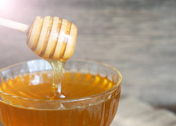 Honey drips from a honey dipper into a beautiful glass bowl. Close-up. Healthy organic thick honey and combs. - Photo, Image