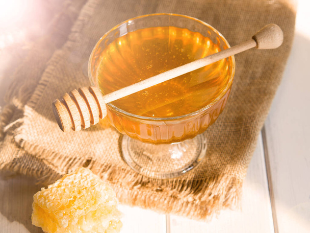 Le miel coule d'une trempette à miel dans un beau bol en verre. Gros plan. Miel épais bio sain et peignes. - Photo, image