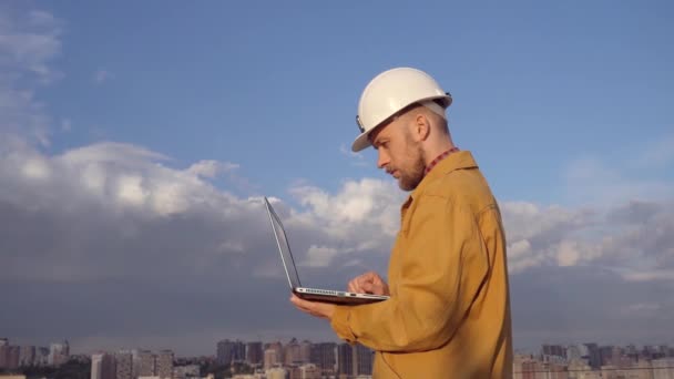 Inspecteur en casque de sécurité utilisant un ordinateur portable sur le chantier de construction - Séquence, vidéo