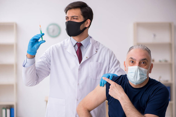 Vieux patient de sexe masculin visitant un jeune médecin en conce de vaccination - Photo, image