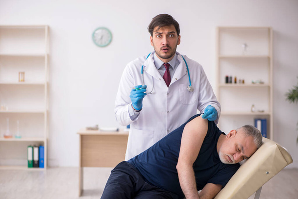 Пациент пожилого возраста посещает молодого врача-мужчину в вакцинации - Фото, изображение