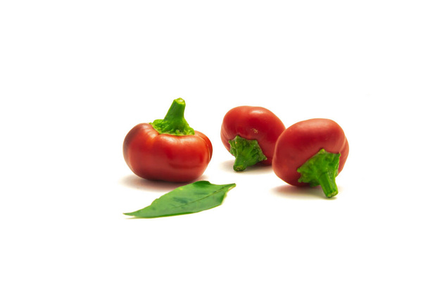Τρεις καυτερές πιπεριές κεράσι ή pimiento φρούτα και φρέσκα φύλλα που απομονώνονται σε λευκό - Φωτογραφία, εικόνα