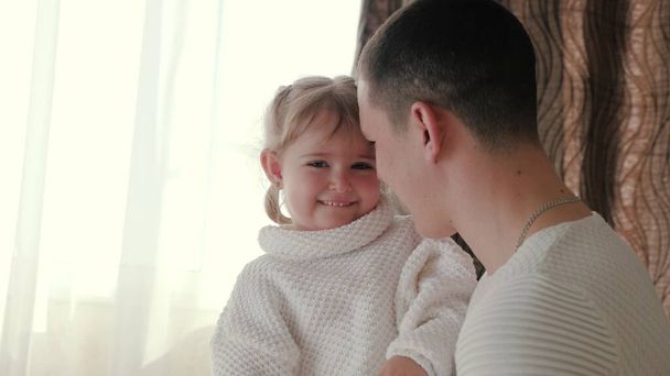 Papai brinca com sua filhinha no quarto, menina abraça seu pai amado em casa pela janela. Família feliz, pai jovem, brinca com pouco bebê adorável, filha sorri alegremente nos braços do pai - Foto, Imagem