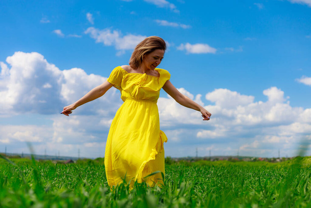 Nuori nainen keltaisessa mekossa ulkona vihreällä pellolla. Käsite ilo raitista ilmaa luonnossa. - Valokuva, kuva