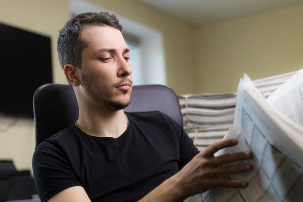 Молодий чоловік читає газету на розмитому офісному тлі
. - Фото, зображення