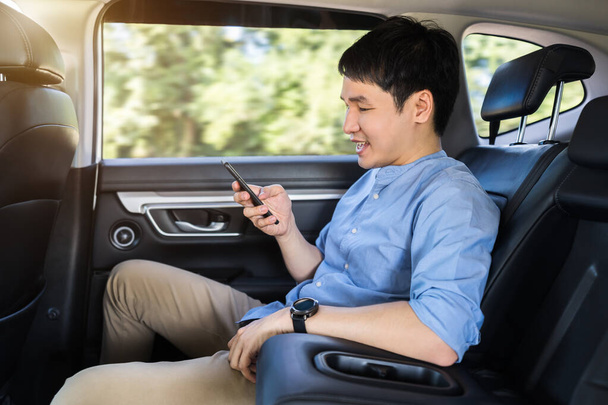 happy young man using a smartphone while sitting in the back seat of car  - Foto, immagini