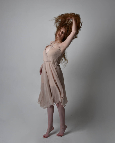 Full length portrait of pretty red haired woman dancer,  wearing skin toned flowing fairy dress. Standing gestural poses  isolated on studio background. - 写真・画像