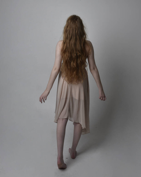 Full length portrait of pretty red haired woman dancer,  wearing skin toned flowing fairy dress. Standing gestural poses  isolated on studio background. - Photo, Image