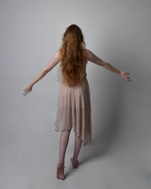 Full length portrait of pretty red haired woman dancer,  wearing skin toned flowing fairy dress. Standing gestural poses  isolated on studio background. - Photo, image
