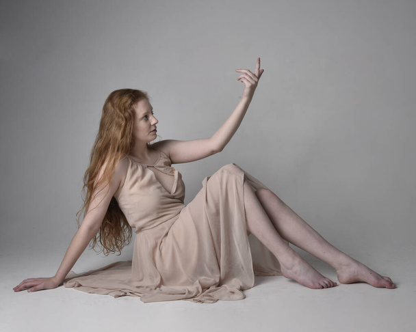 Retrato de cuerpo entero de una bailarina pelirroja bonita, con piel tonificada vestido de hada que fluye. Posturas gestuales sentadas aisladas en el fondo del estudio. - Foto, imagen