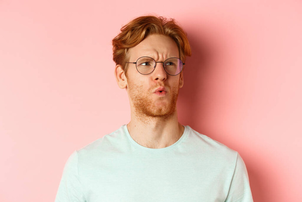 Ouch thats bad. Face of redhead man showing pity and feeling sorry for someone, frowning and looking with compassion, standing over pink background - Photo, Image
